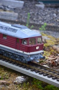 Close-up of a detailed red miniature train on a scenic model railway track outdoors.